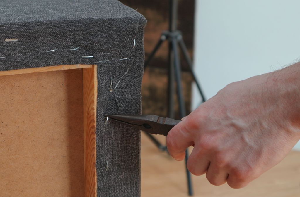 A person is using a pair of pliers to fix a piece of furniture.