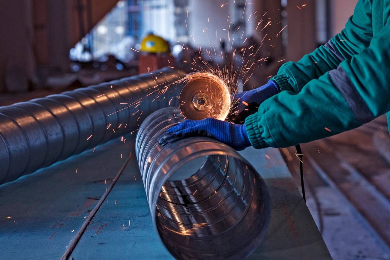 A person is grinding a metal pipe with a grinder.