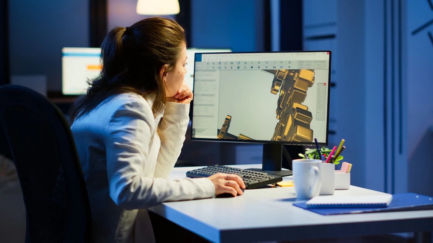 A woman is sitting at a desk looking at a computer screen.