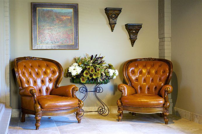 Two tan leather armchairs flanking a floral arrangement on a metal table in a beige room