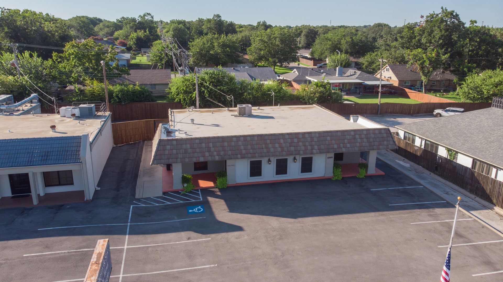 Aerial view of a small commercial building with a parking lot and trees in the background.