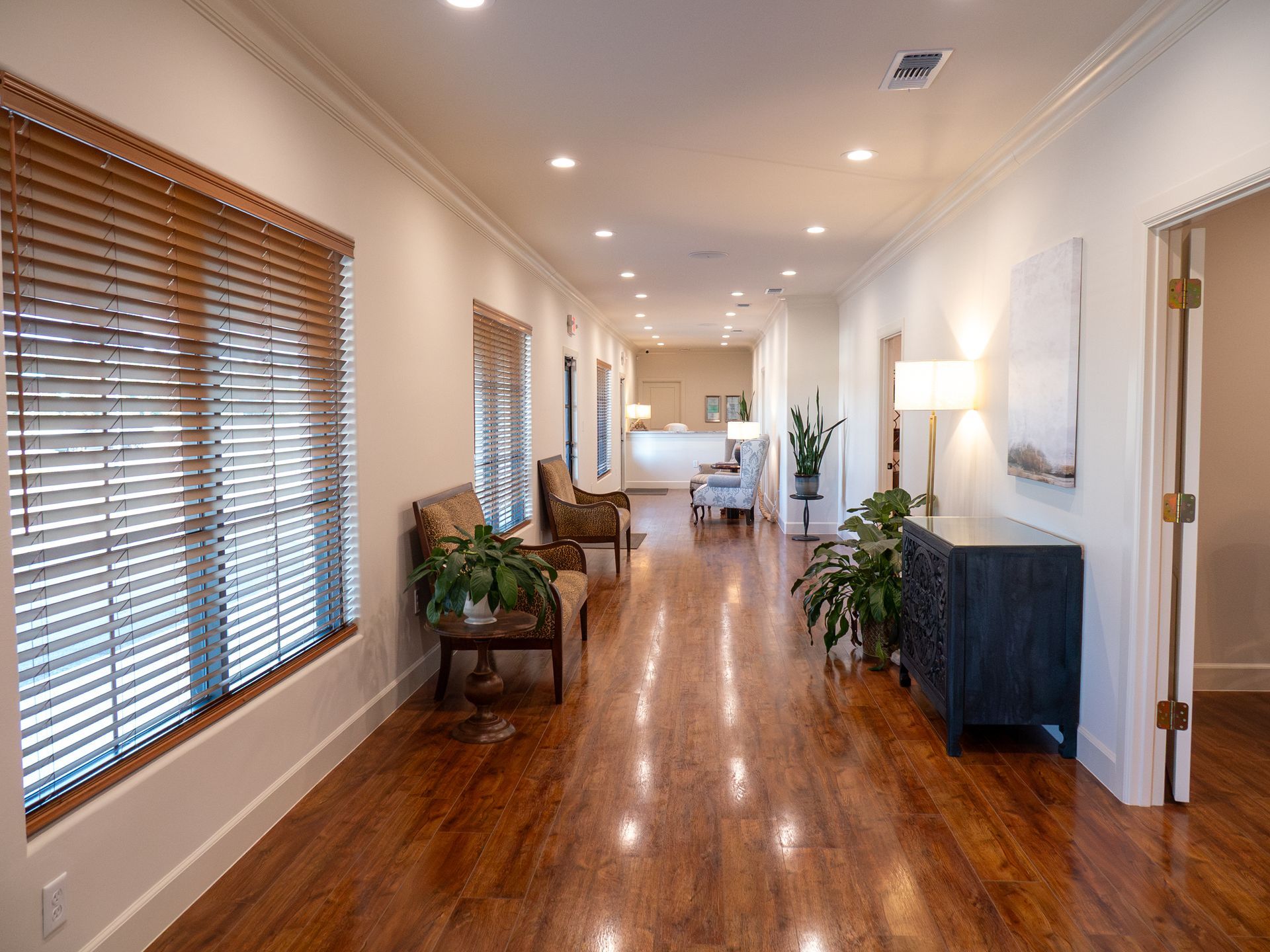 Bright hallway with wood floors, window blinds, plants, lamp, and seating in a modern interior.