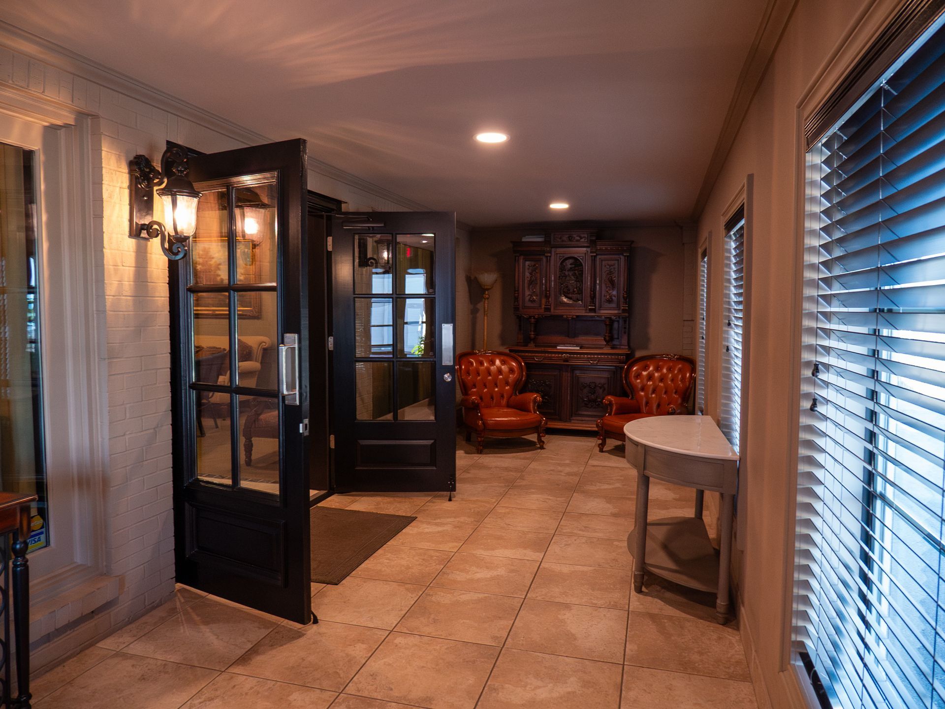 Elegant hallway with tiled floor, glass doors, and warm seating area in the distance
