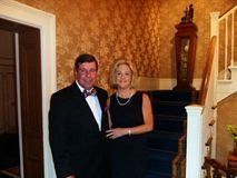 Couple posing in formal attire at the bottom of a staircase in a warmly lit home interior