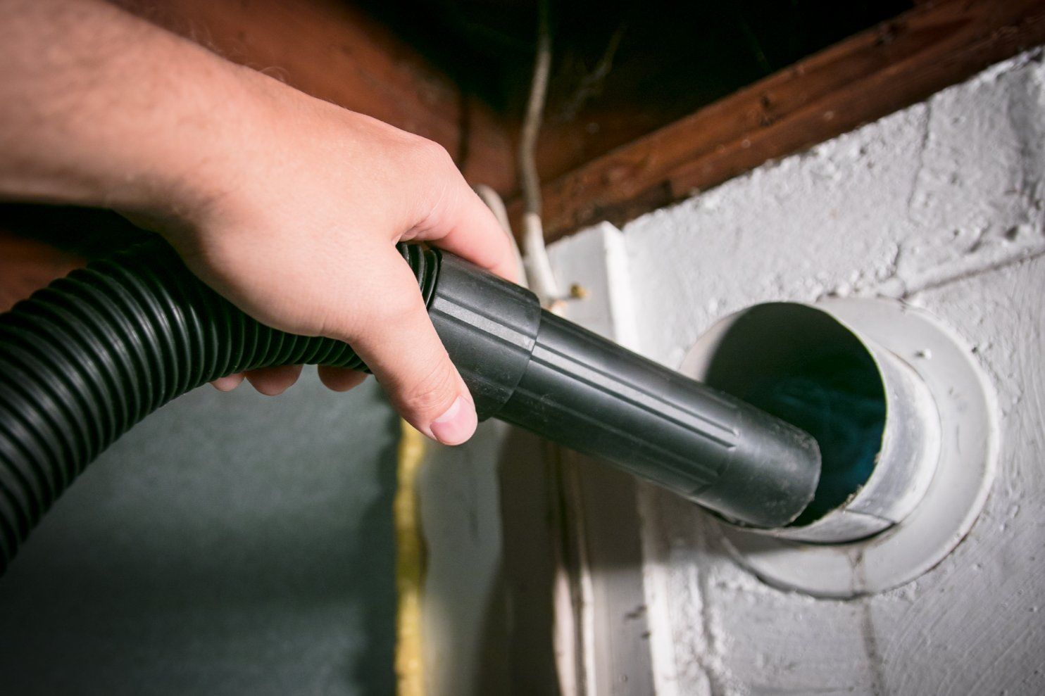 Hand vacuuming a dryer vent in a white painted wall.