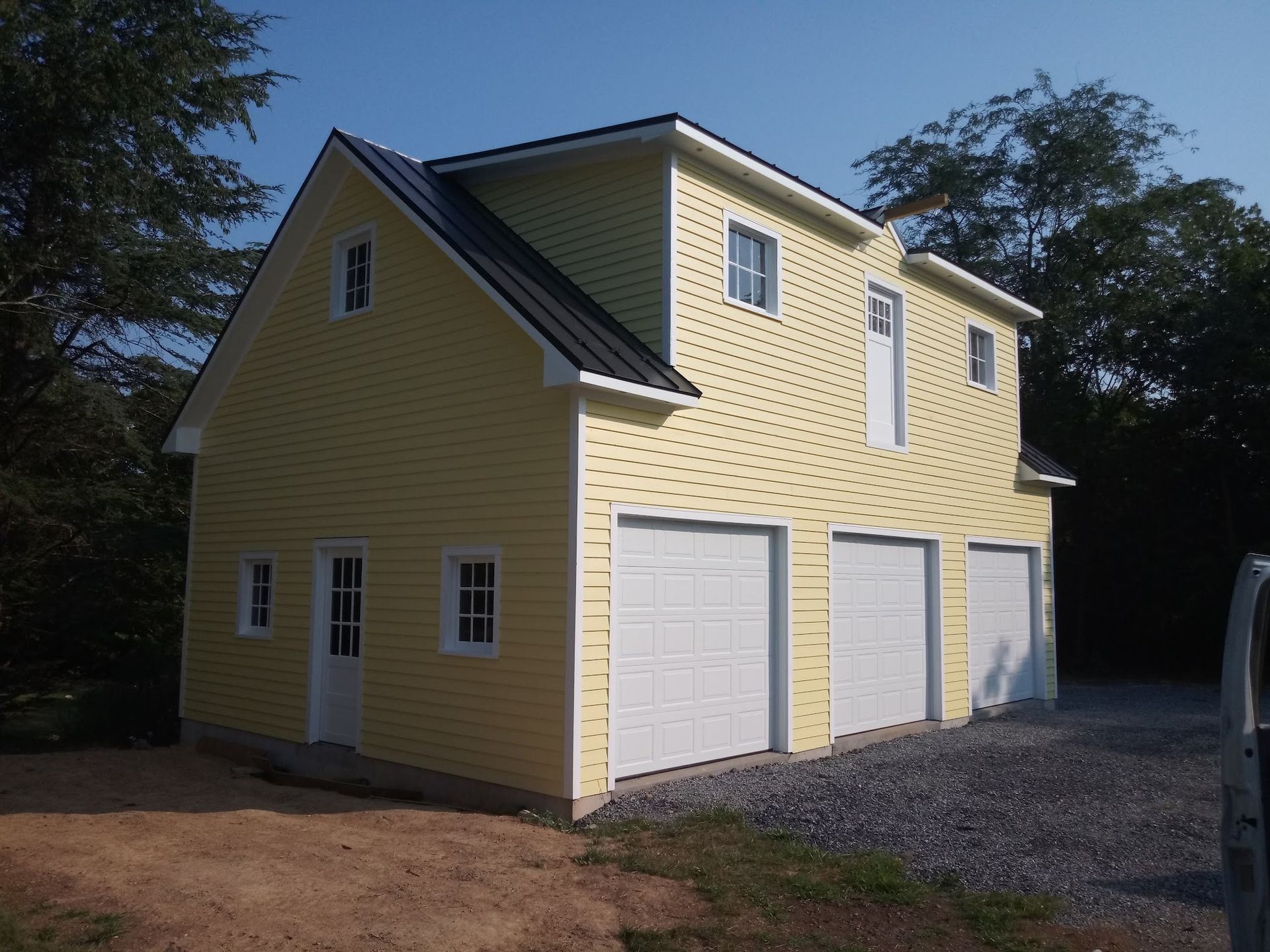Yellow three-car garage with black roof and small windows, set on a gravel driveway.
