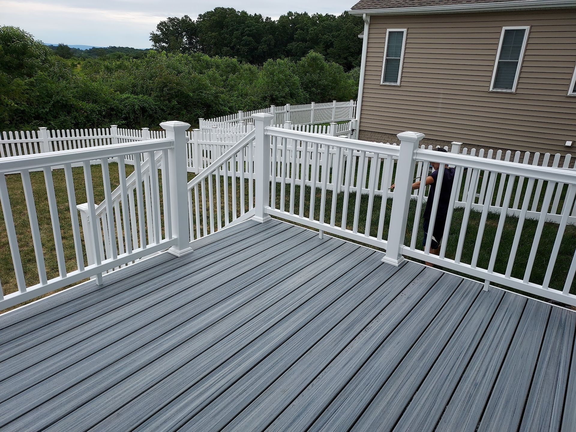 Gray composite deck with white railing surrounding a backyard, partial view of a house.