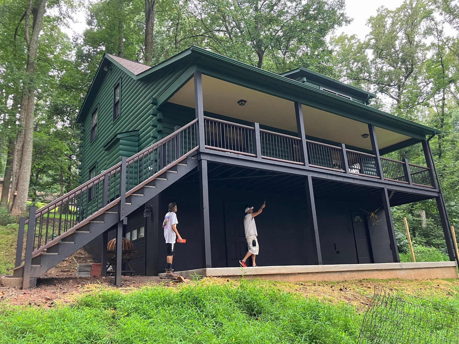 Green cabin with black trim, a large porch, and two people playing outside.