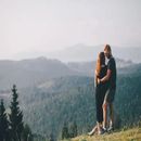 Two people standing close together on a mountain overlook, gazing at misty forested hills