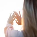 Person raising hands toward bright sunlight, with a blurred background