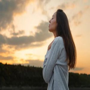 Woman in a gray sweater standing in profile at sunset, looking toward the horizon.