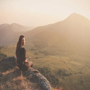 Person sitting on a rocky overlook, gazing over a sunlit mountain valley at sunset
