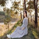 Woman in a white floral dress sitting on grass in a wooded field at sunset