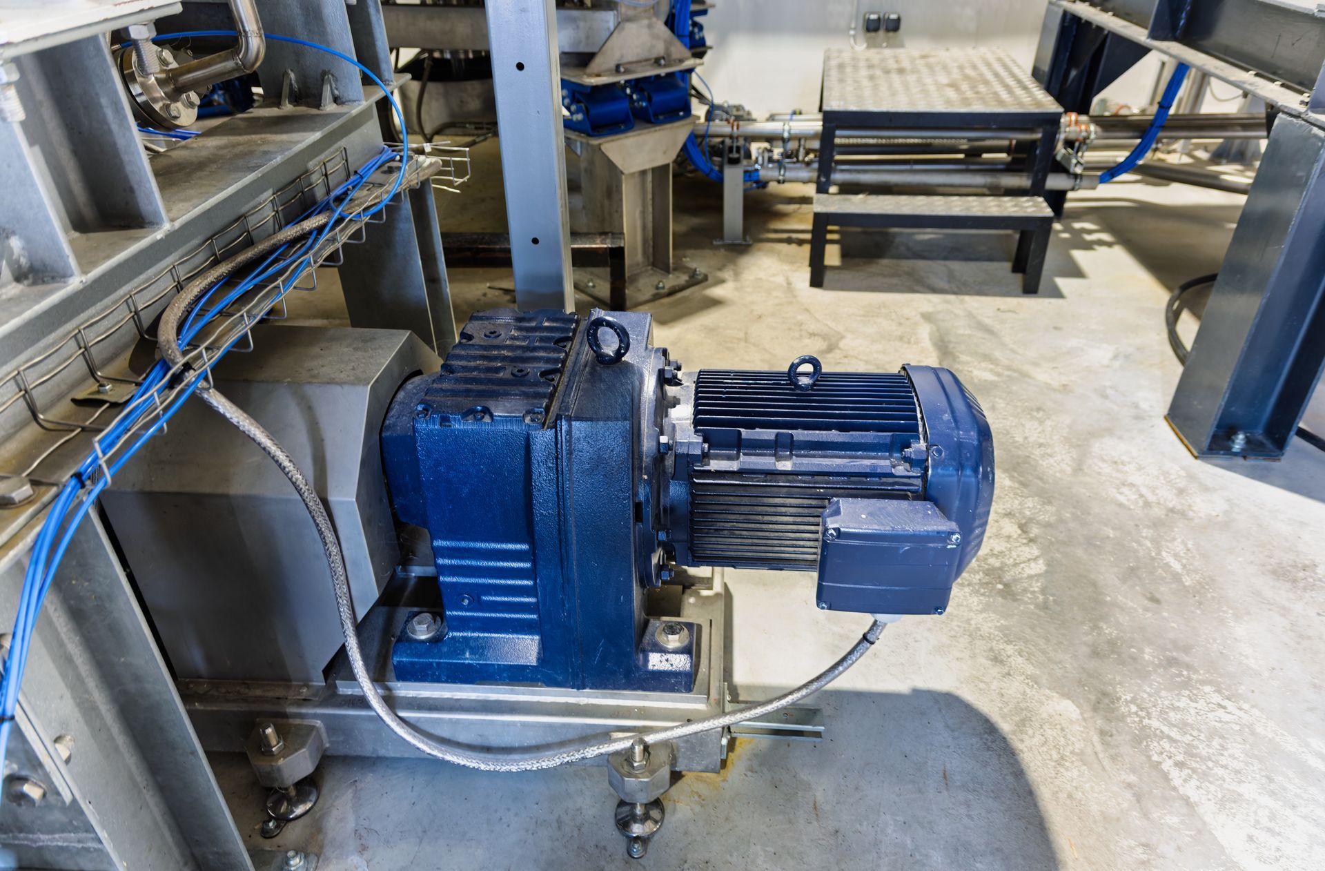 A large commercial food mixer stands near shelves holding assorted industrial motors and pumps in a warehouse. A large commercial food mixer stands near shelves holding assorted industrial motors and pumps in a warehouse.