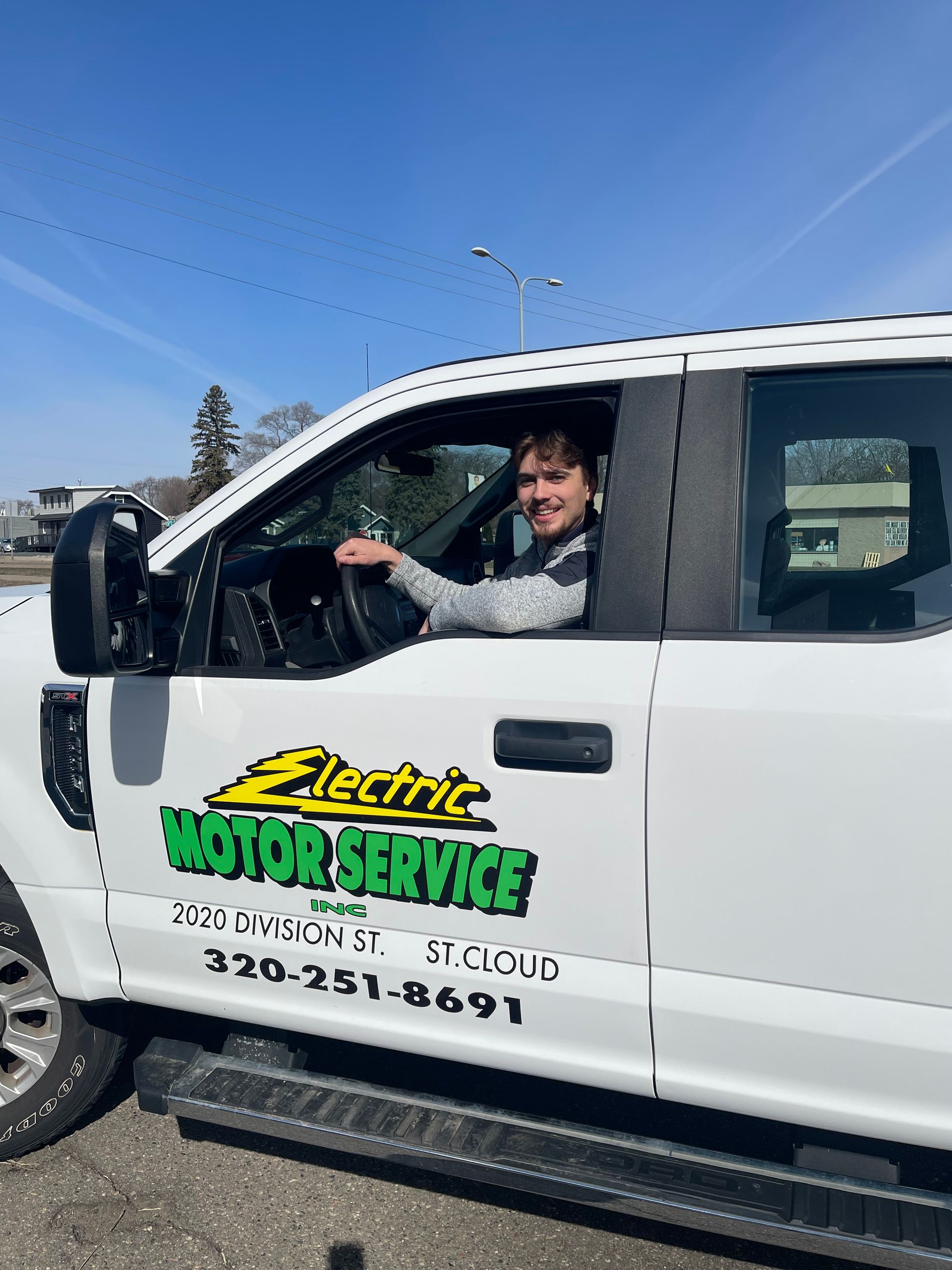 A person sits in the driver’s seat of a white service truck labeled A person sits in the driver’s seat of a white service truck labeled