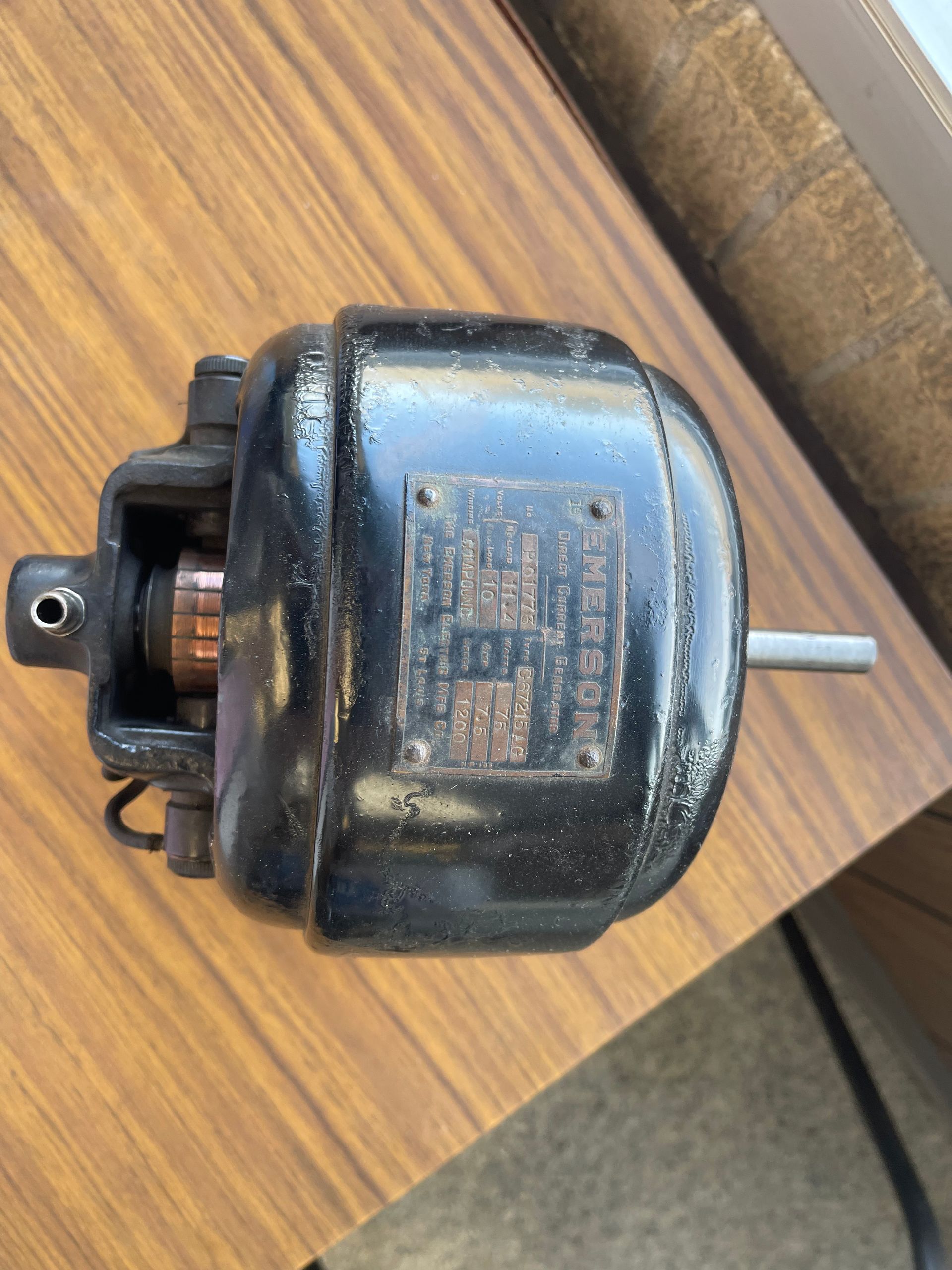 A small, black electric motor sits on a wooden table, showing a copper commutator and a metal information plate. A small, black electric motor sits on a wooden table, showing a copper commutator and a metal information plate.