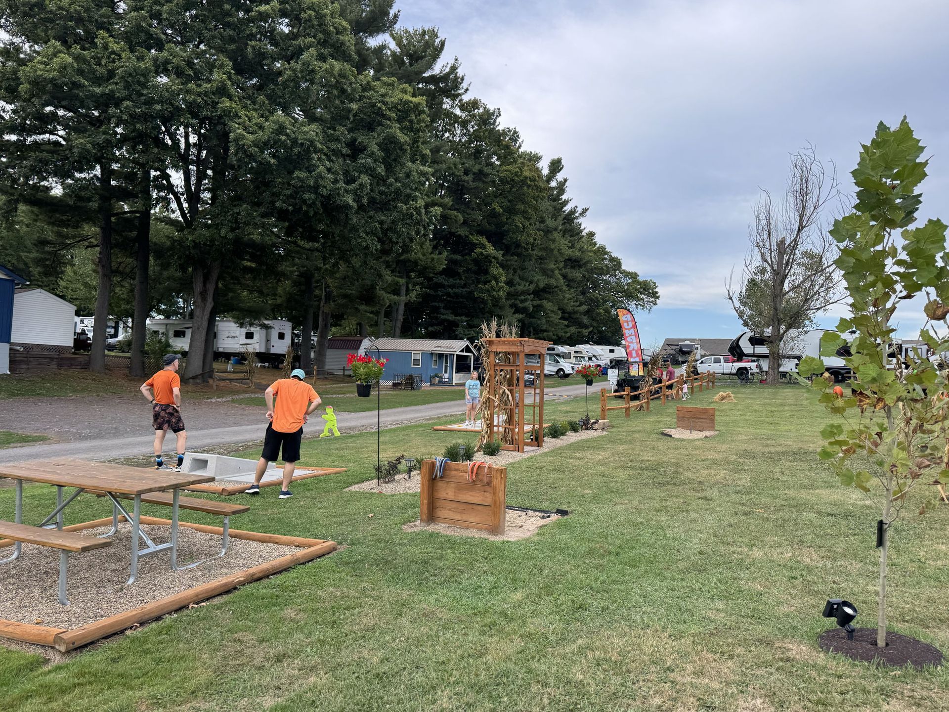 Two people in orange shirts near a campsite, landscaping in progress with flower boxes.