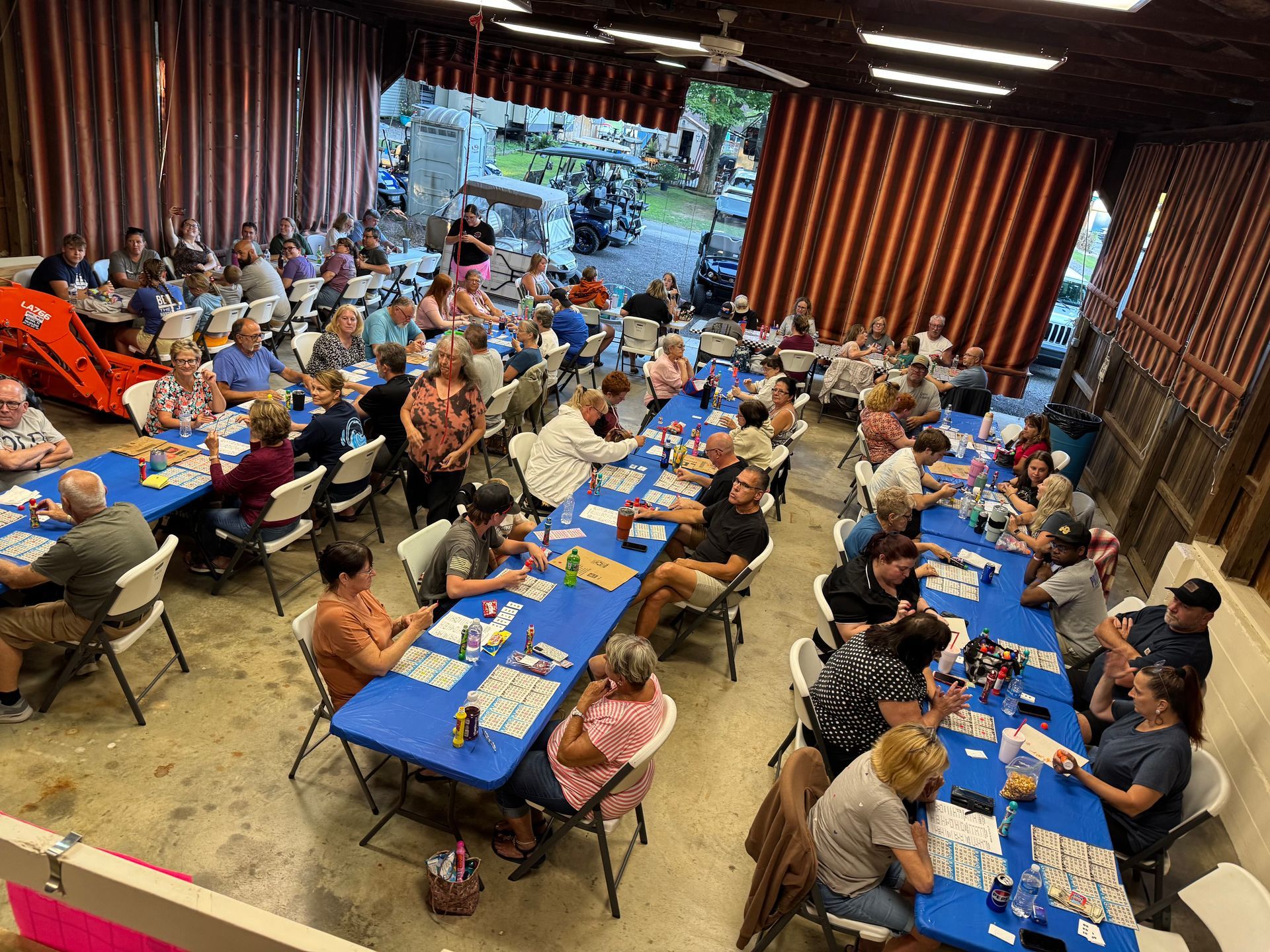 Large group of people playing bingo at long tables in a building, with cards and chips visible.