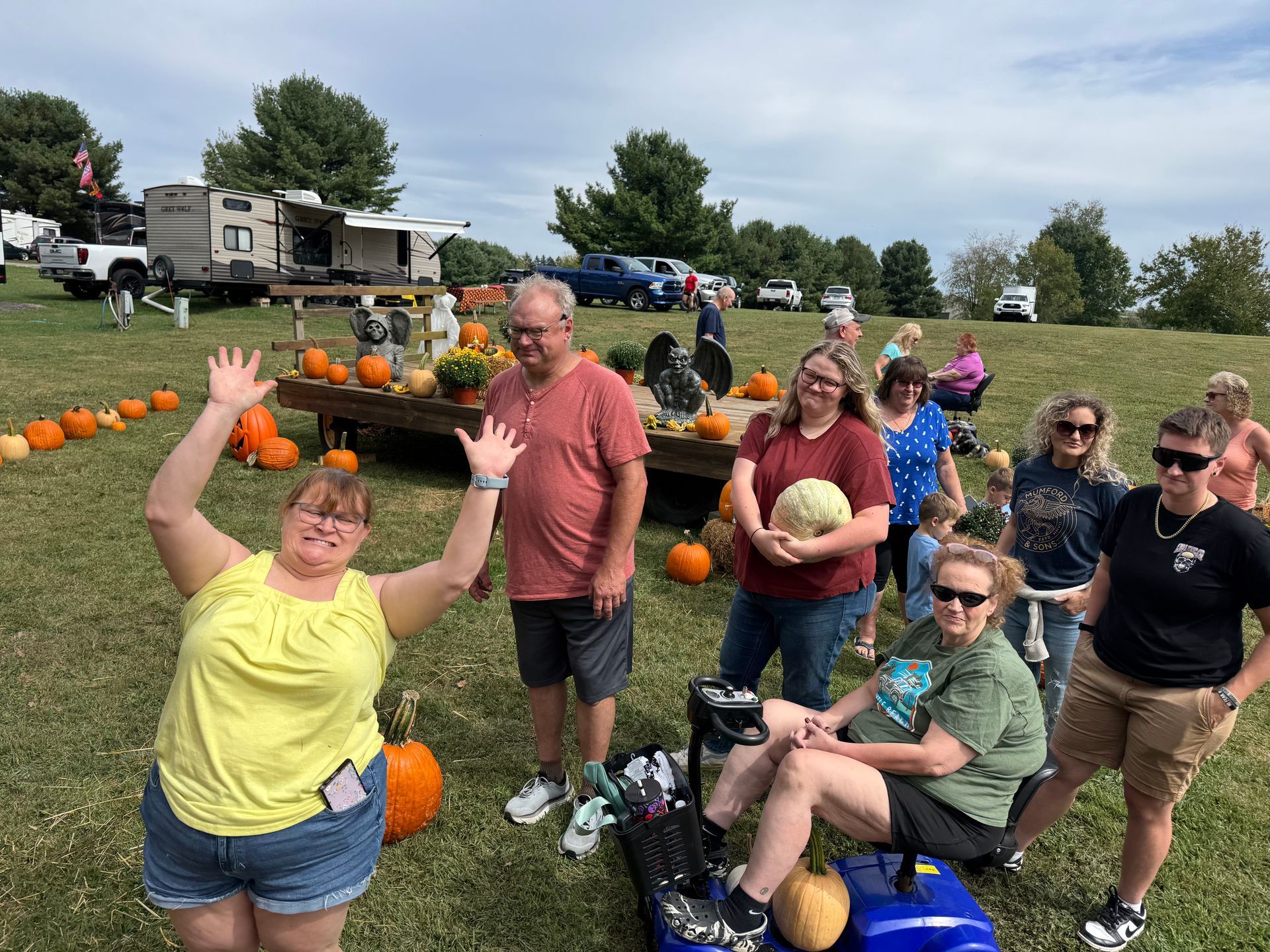 Group of people in a pumpkin patch. One woman waves enthusiastically.