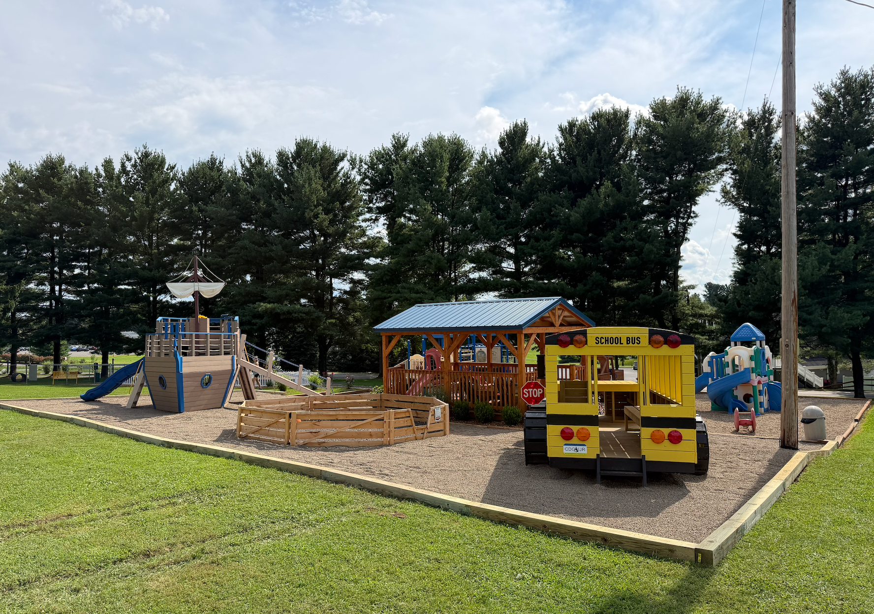 Playground with slides, swings, and kids, surrounded by grass and trees.