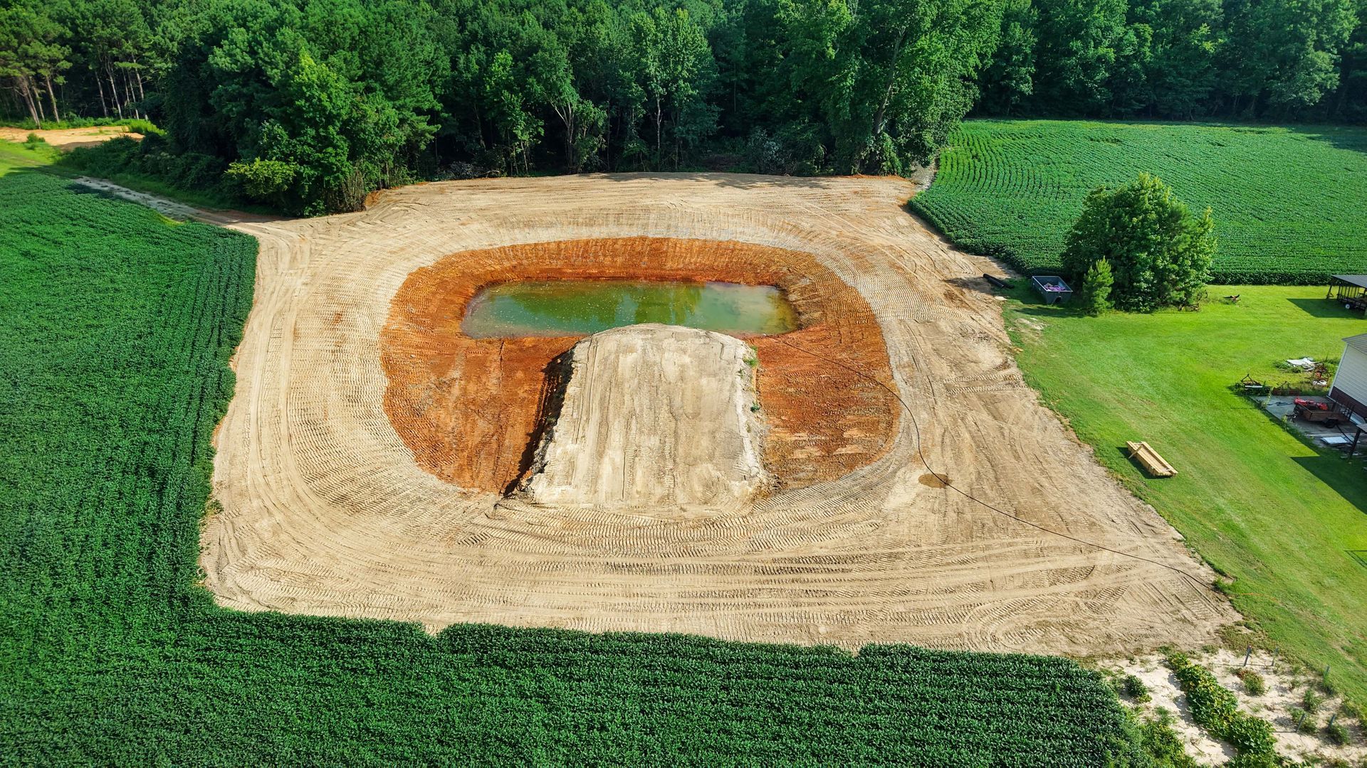 Aerial view of a newly constructed pond surrounded by dirt and fields of crops and grass.
