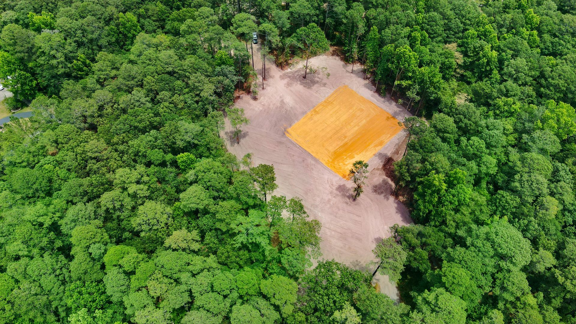 Aerial view of deforested area within a green forest, with a square of orange soil in the clearing.