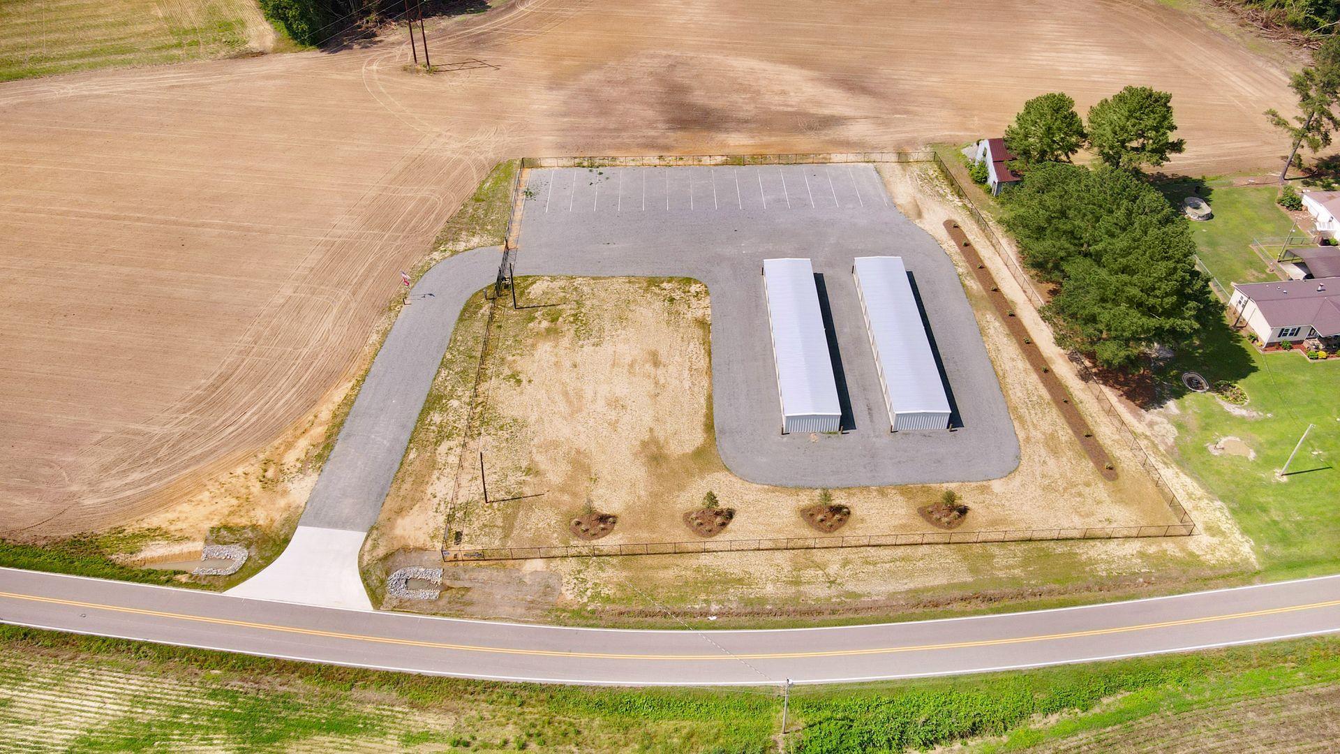 Aerial view of two silver storage buildings on a gravel lot next to a road and a field.