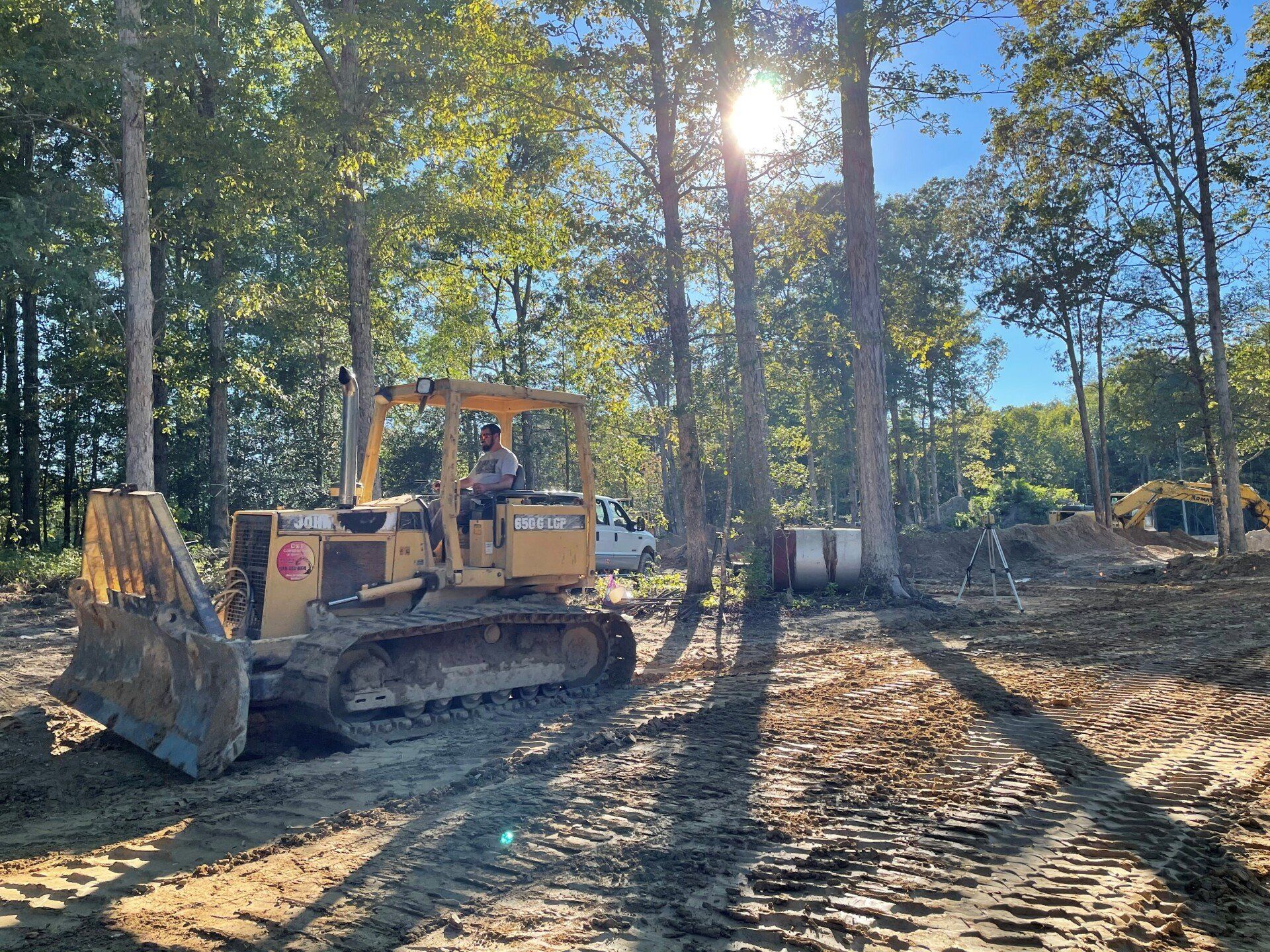 Yellow bulldozer clearing land in a wooded area with a sunny sky.