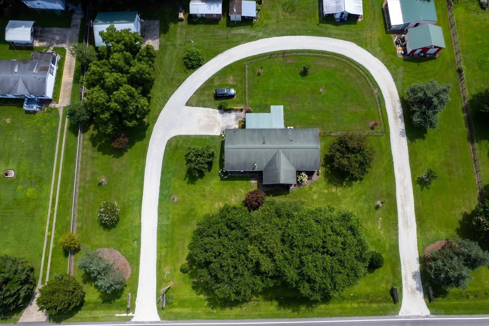 Aerial view of a house with a curved driveway surrounded by green grass and trees in a rural setting.