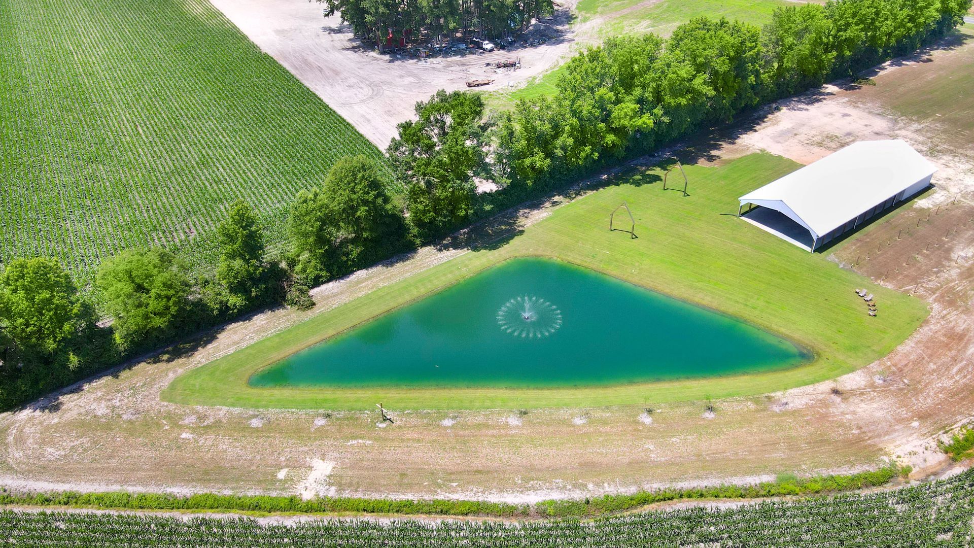 Aerial view of a teal-colored pond, lush green grass, trees, and a white-roofed building on a farm.