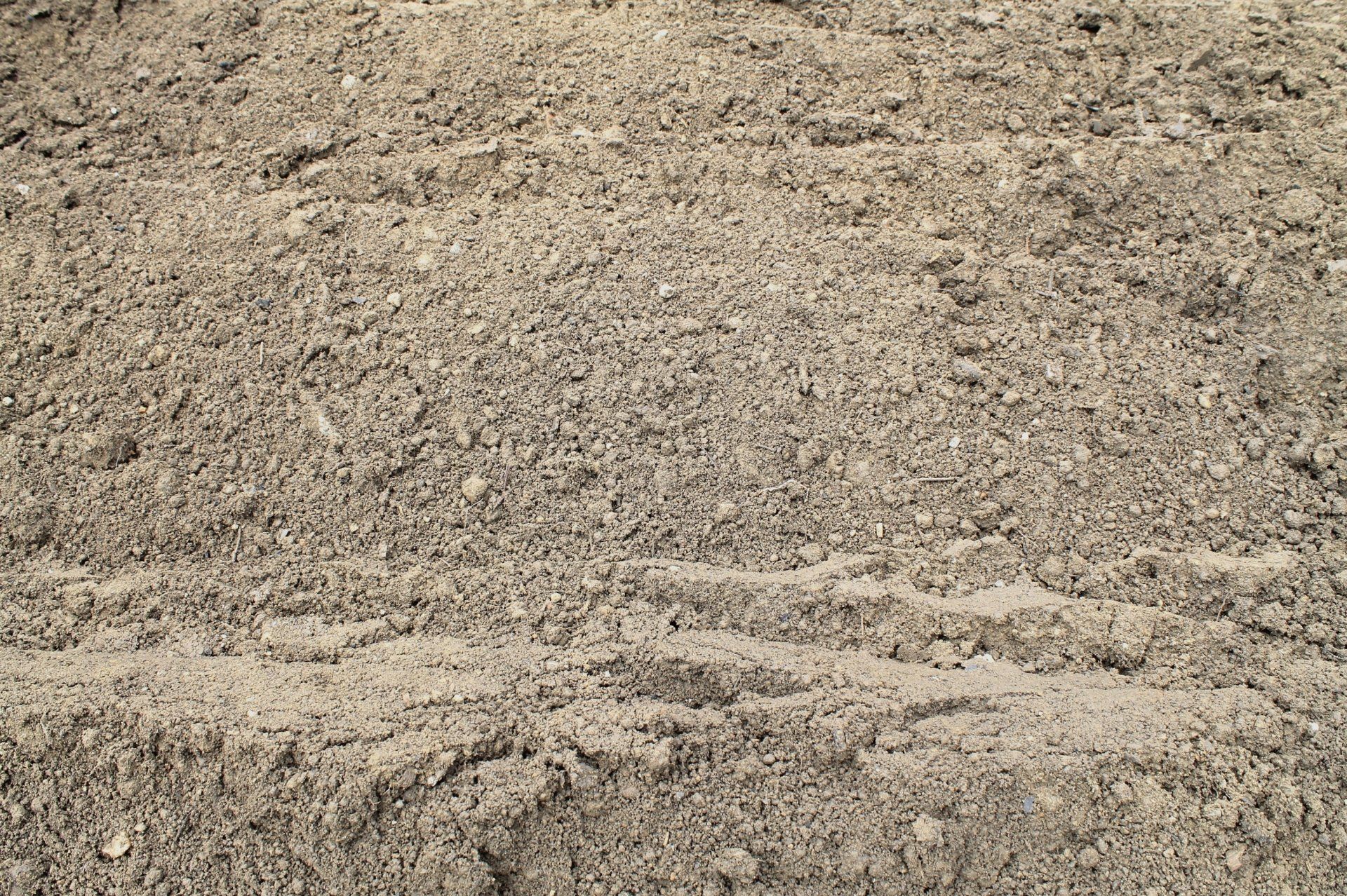 Pile of light brown sand, textured surface, outdoors.