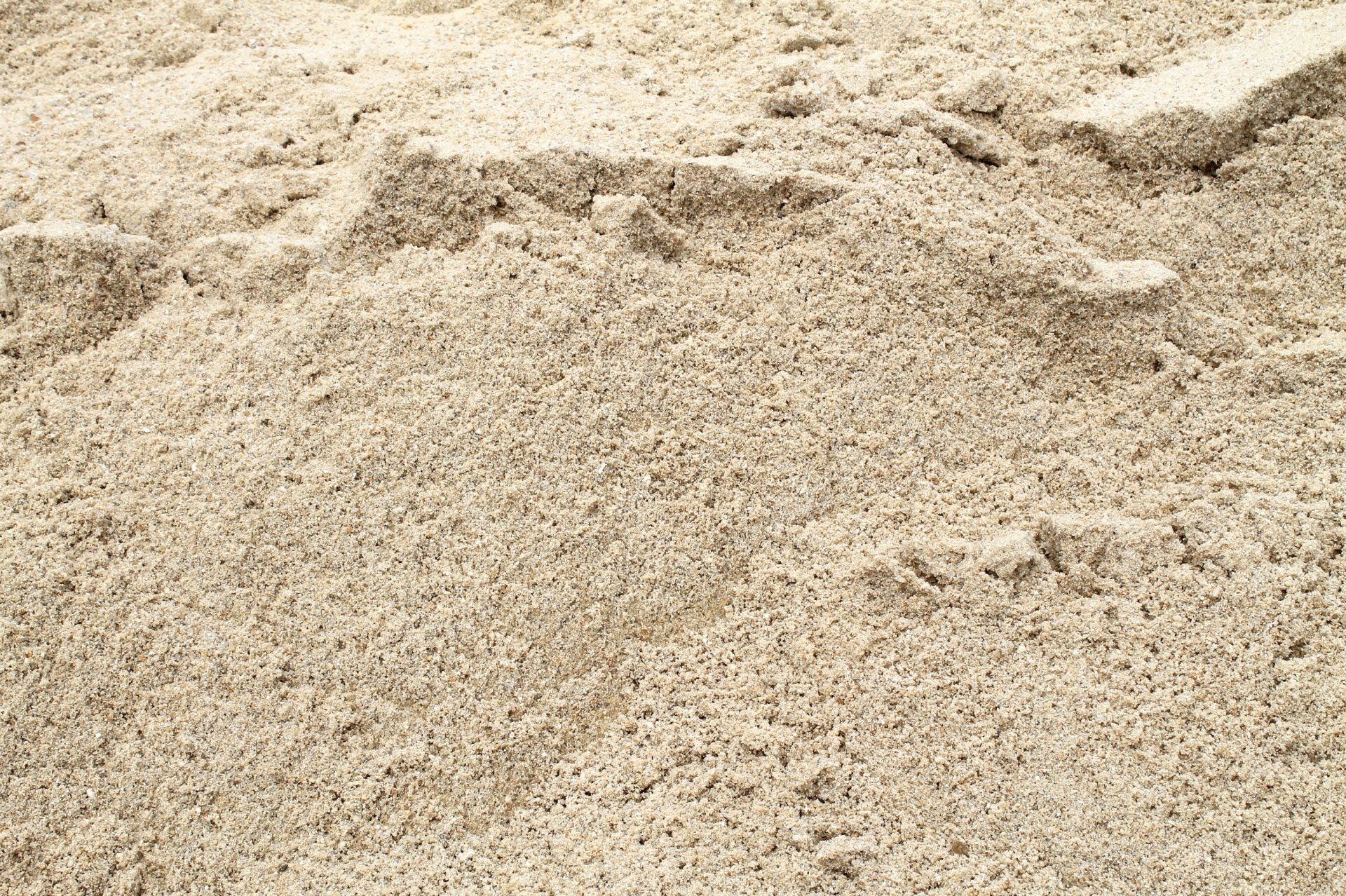 Tan sand pile, close-up view. Rough texture with variations in color.