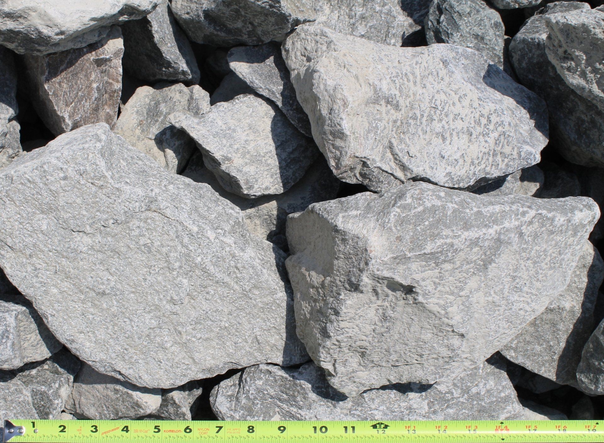 Rough, gray landscaping rock, varying sizes, piled on the ground.