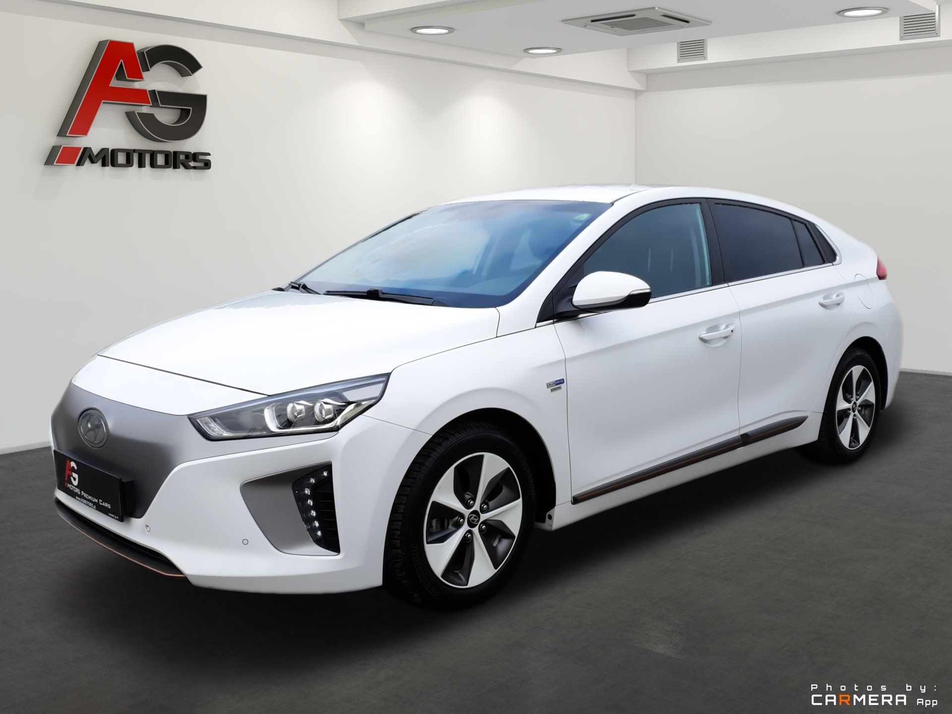 White compact hatchback sedan displayed in a showroom, front-left view