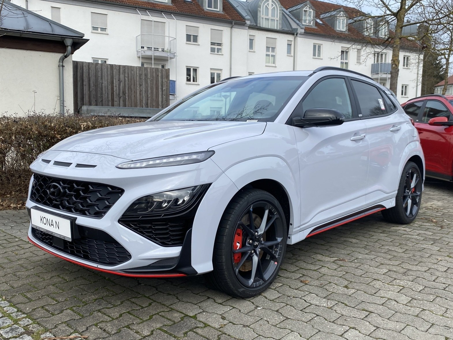 Silver sporty SUV parked on cobblestone street, with black wheels and red trim, in front of houses
