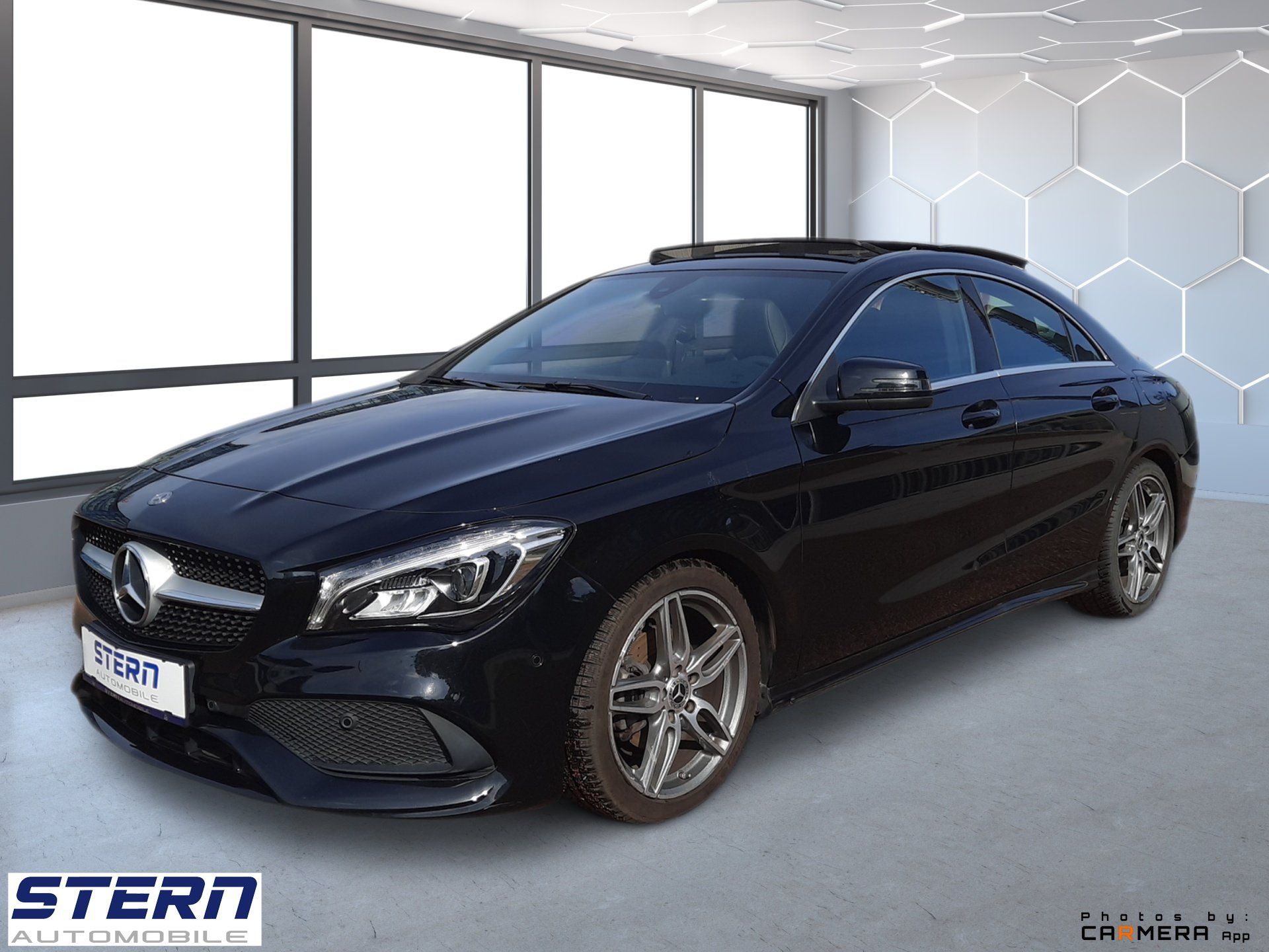 Čierny sedan Mercedes-Benz v showroome s veľkými oknami a bielym šesťuholníkovým vzorom na stene