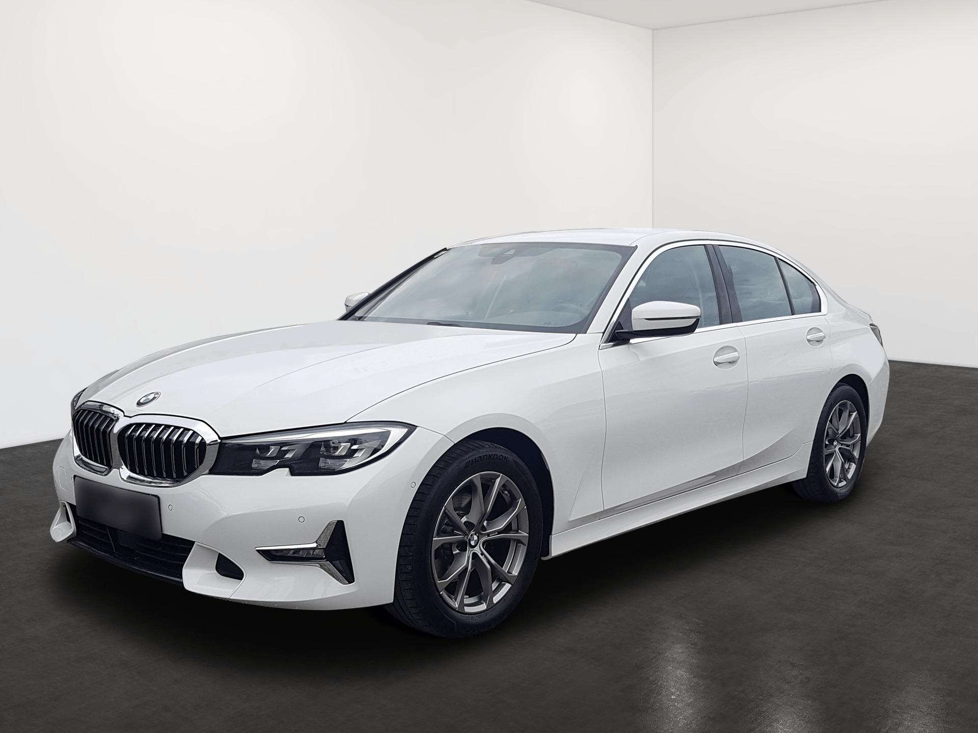 White BMW sedan parked in a studio-like room with a dark floor and white walls