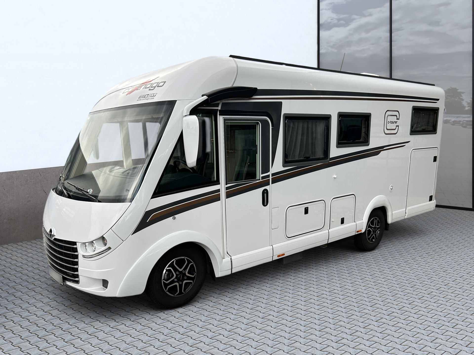 Biely obytný automobil zaparkovaný na spevnenom povrchu, zobrazený v bočnom pohľade na rovnom pozadí