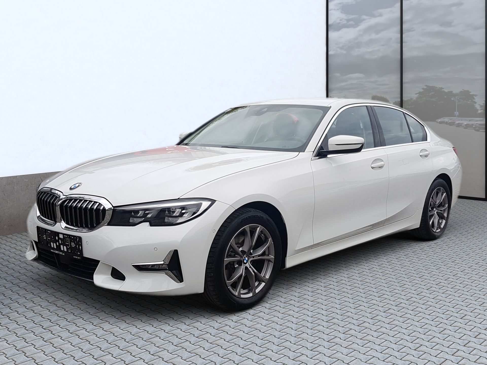 White BMW sedan parked on a paved lot beside a glass building
