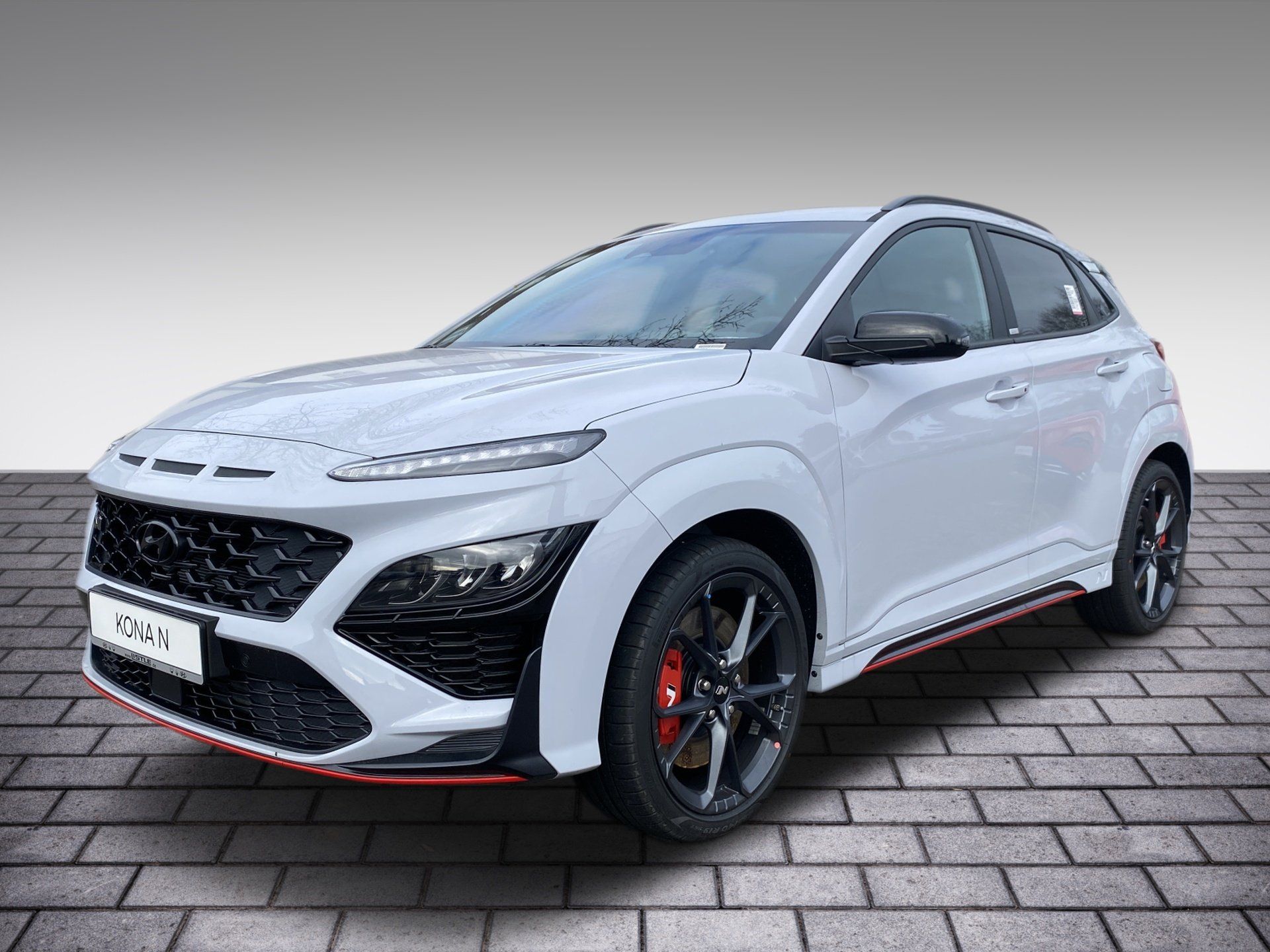 White sporty hatchback on brick pavement, front-left view, with red accents and black wheels.