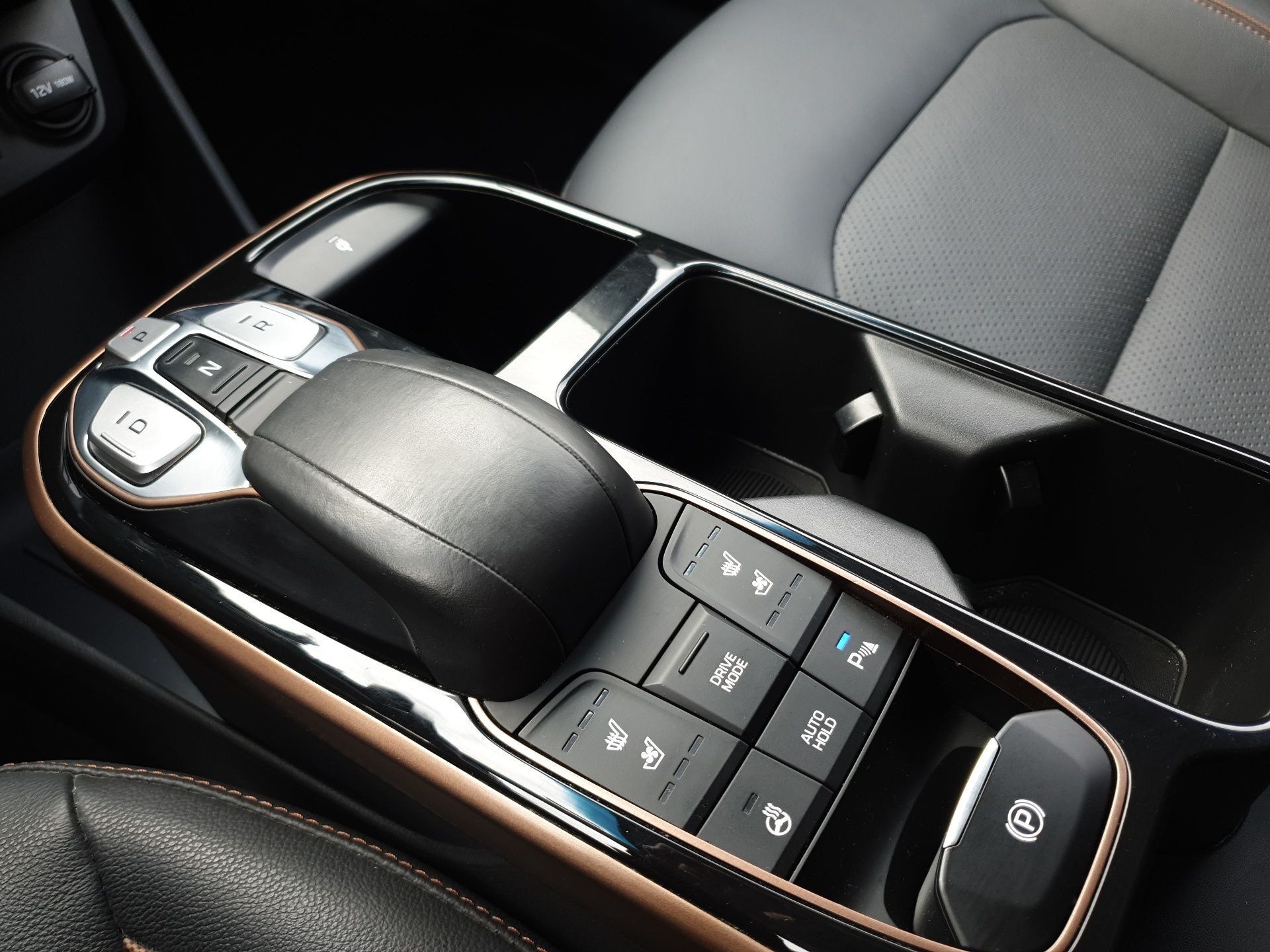 Car center console with gear selector, buttons, and storage compartment in black and silver trim