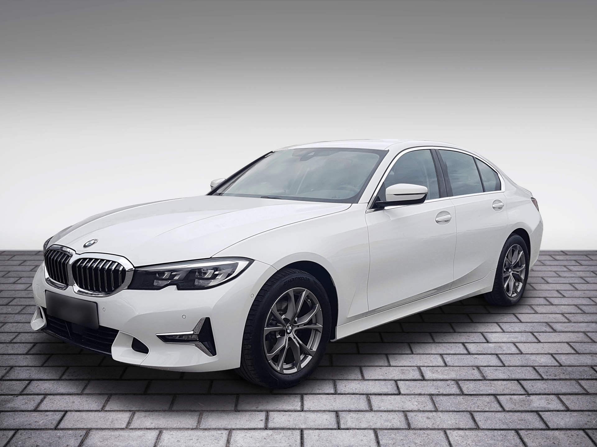 White BMW sedan parked on gray brick pavement, front-left view.