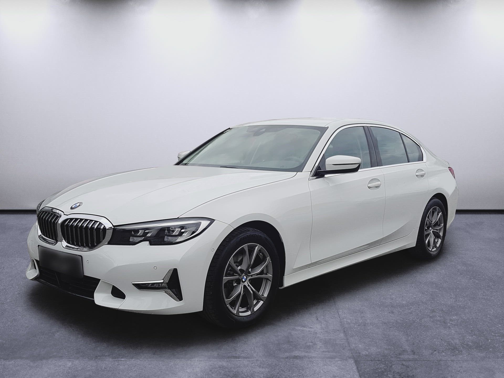 Biely sedan BMW v štúdiu, zobrazený vľavo spredu na sivej podlahe s jednoduchým svetlým pozadím