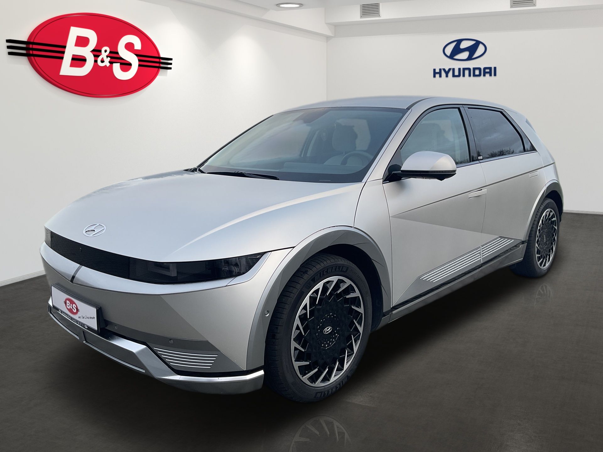 Strieborný elektrický hatchback Hyundai v showroome s logami B&S a Hyundai na stene