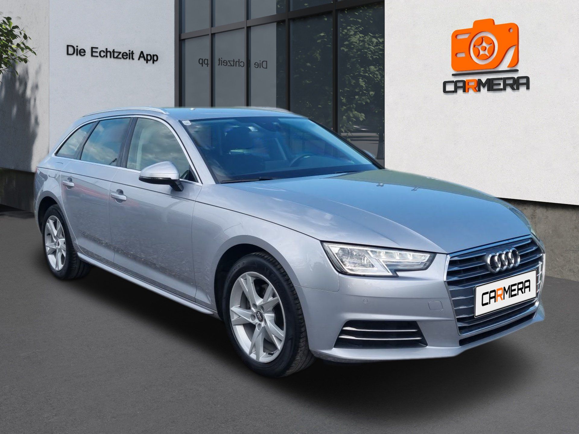 Strieborný sedan Audi zaparkovaný pred obchodom s fotoaparátmi.