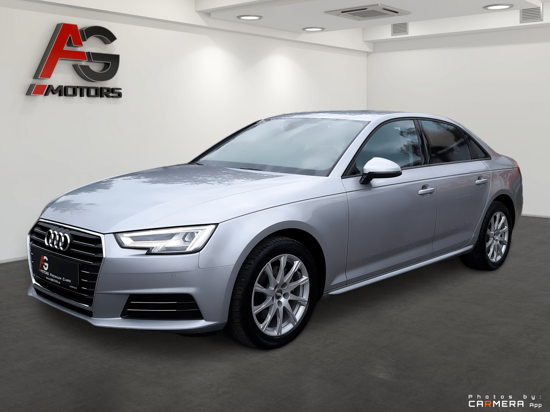 Strieborný sedan Audi zaparkovaný v showroome, pohľad zľava spredu.
