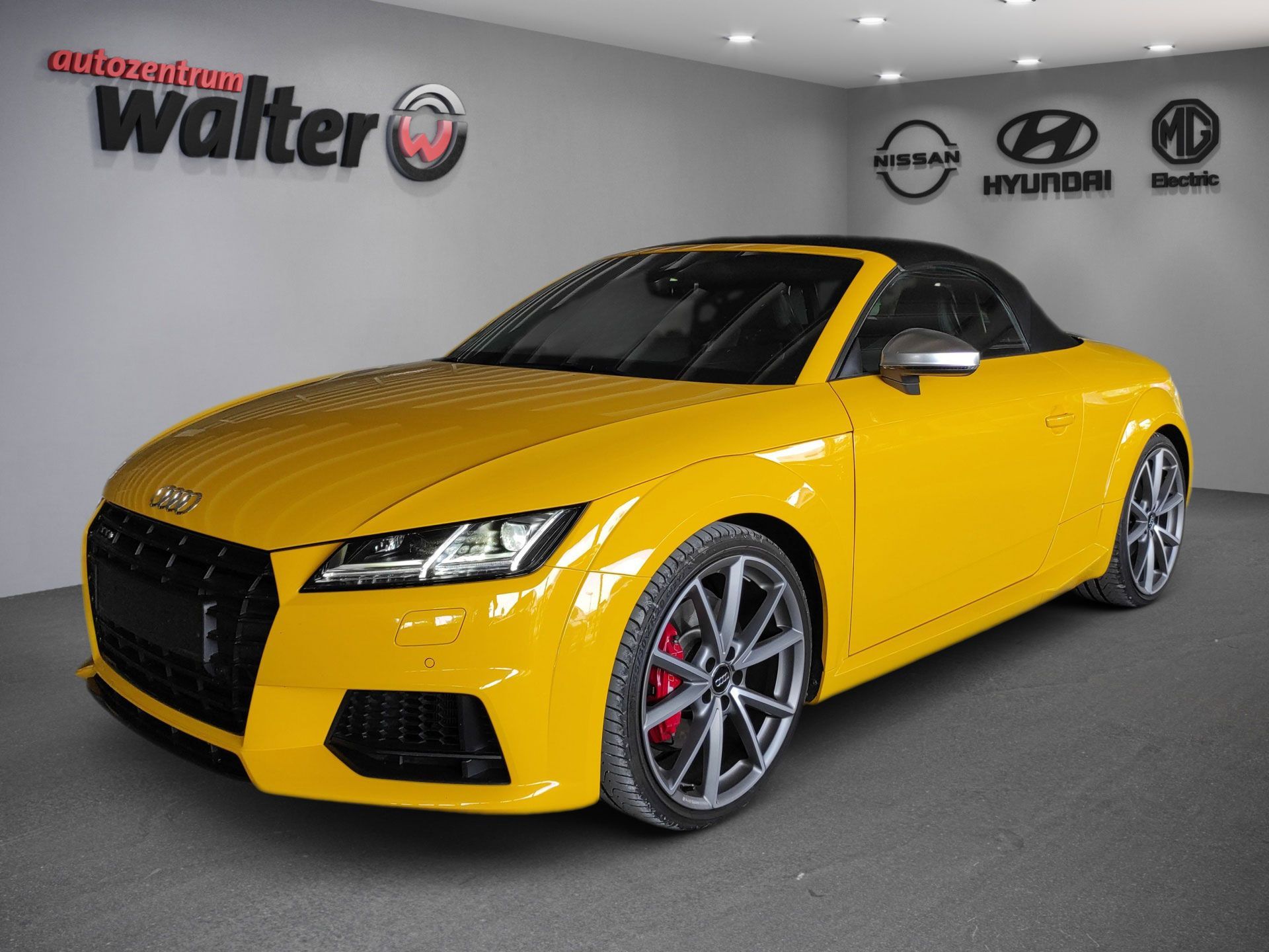 Yellow Audi sports coupe in a showroom, angled front view with black roof and silver wheels