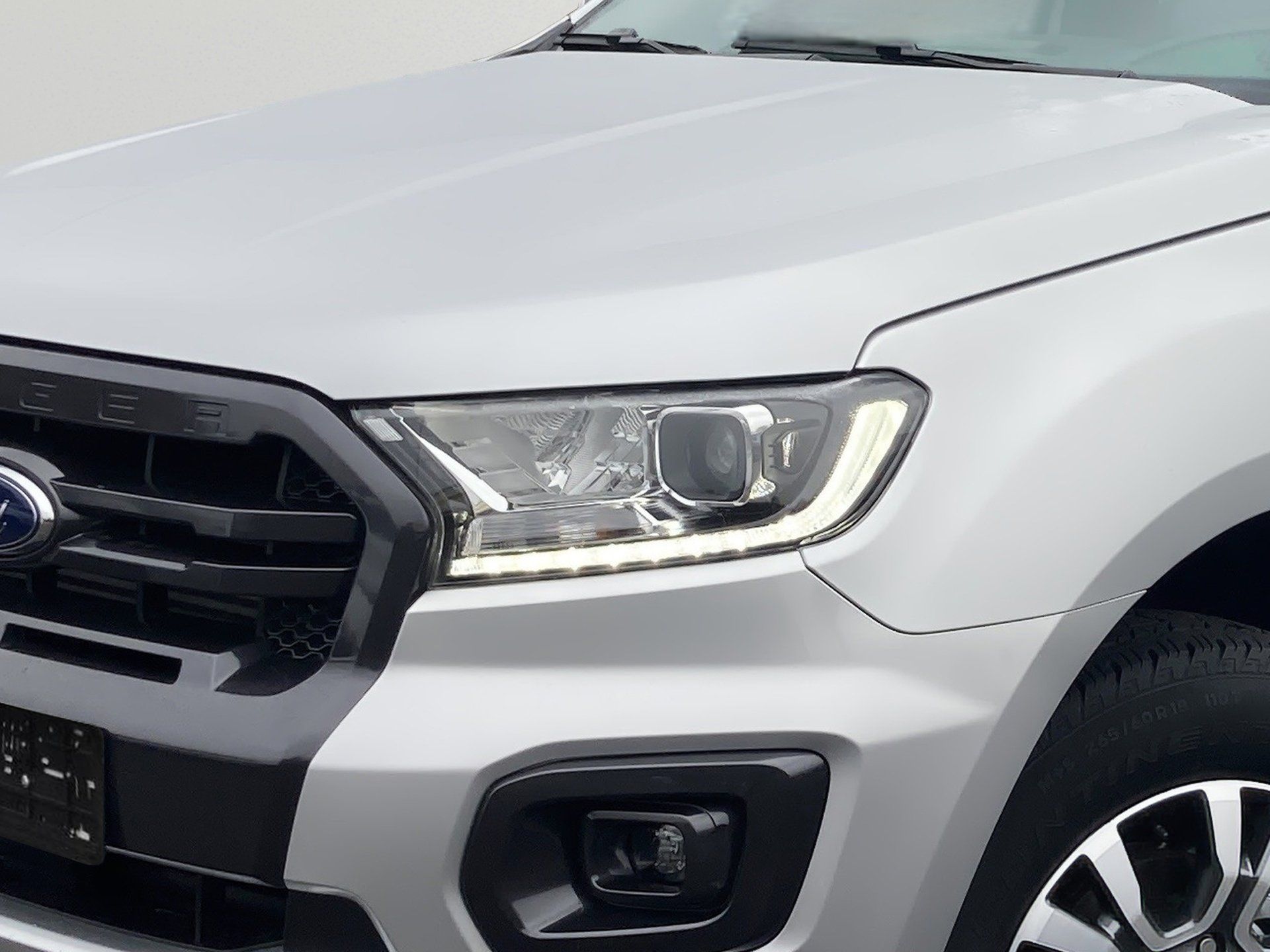 Strieborná predná časť SUV s mriežkou, svetlometmi a detailným záberom na koleso