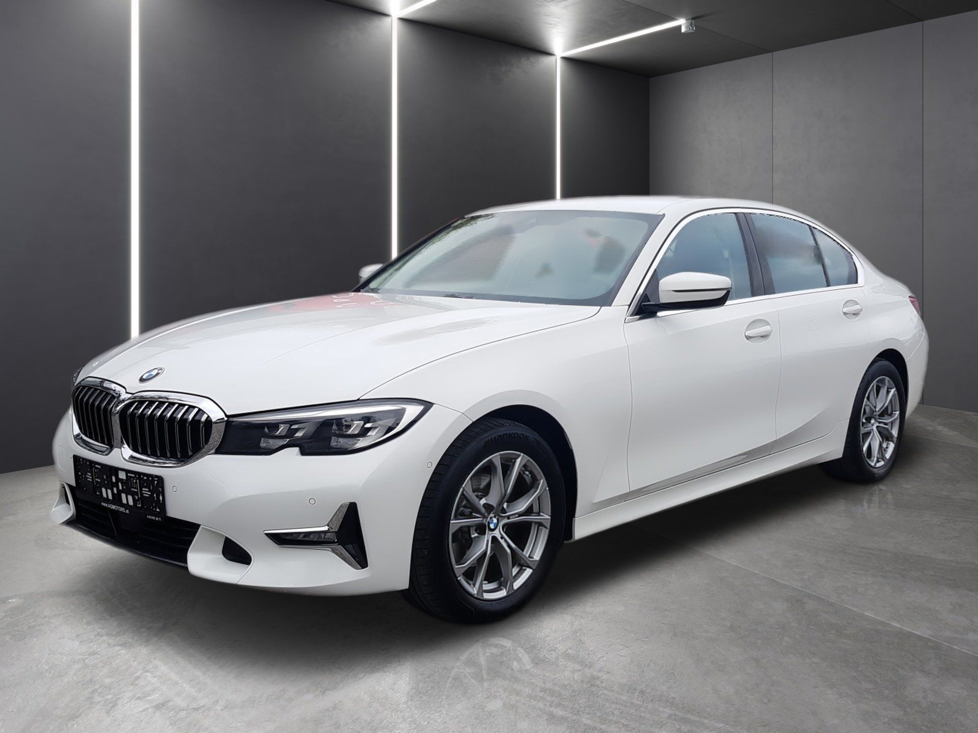 Biely sedan BMW v sivom štúdiu, pohľad spredu z troch štvrtín s moderným osvetlením