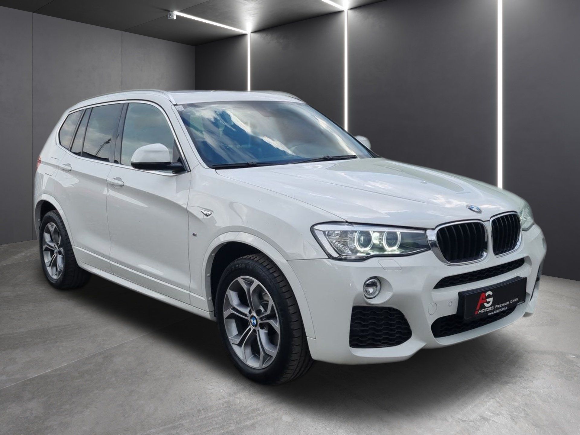 Biele SUV BMW v štúdiovom prostredí s tmavými stenami a vertikálnymi svetelnými pásmi
